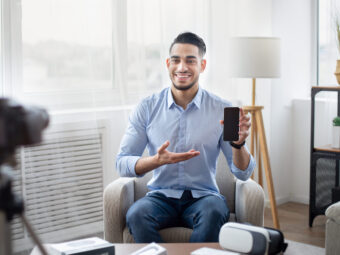 Arab male influencer filming video review of contemporary smartphone on dslr camera at home, mockup on screen