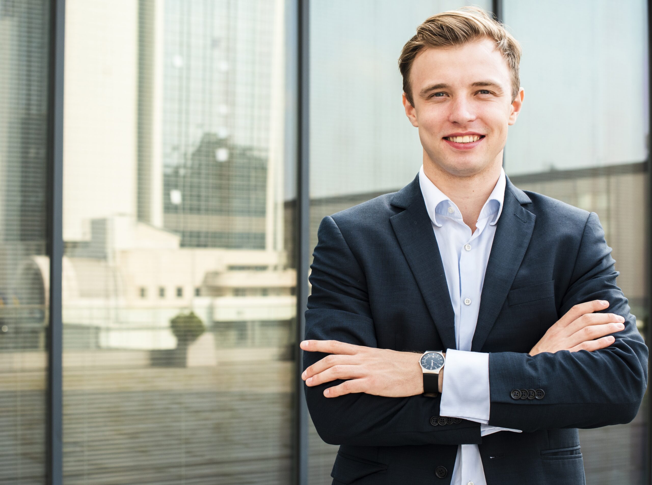 laechelnder-geschaeftsmann-mit-den-gekreuzten-armen-die-kamera-betrachten